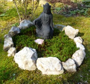 A circle of milky quartz stone in moss around a black lava Kwan Yin.